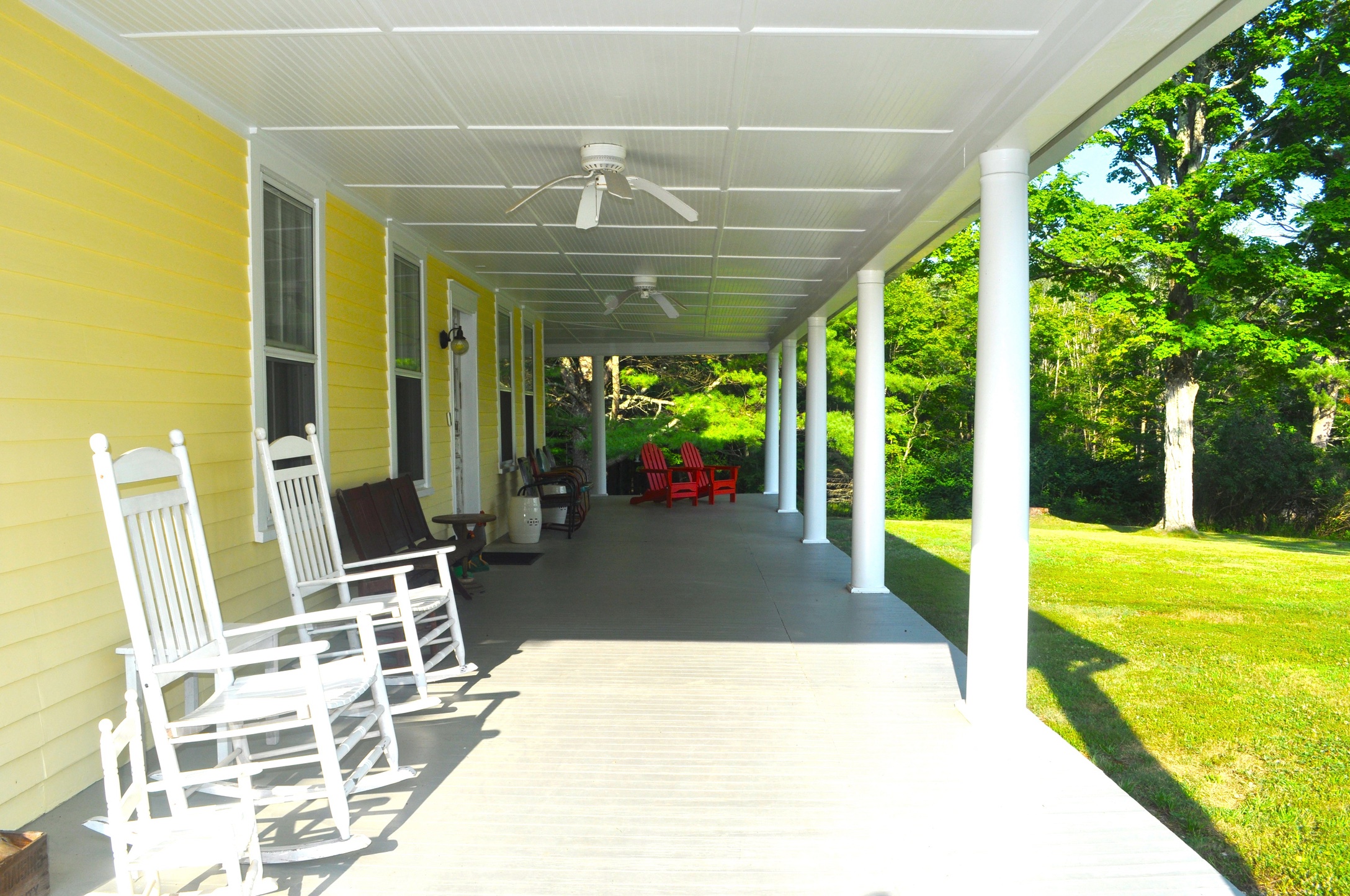 The wrap-around porch looking along its length, furnished with teak benches and chairs and overhead ceiling fans
